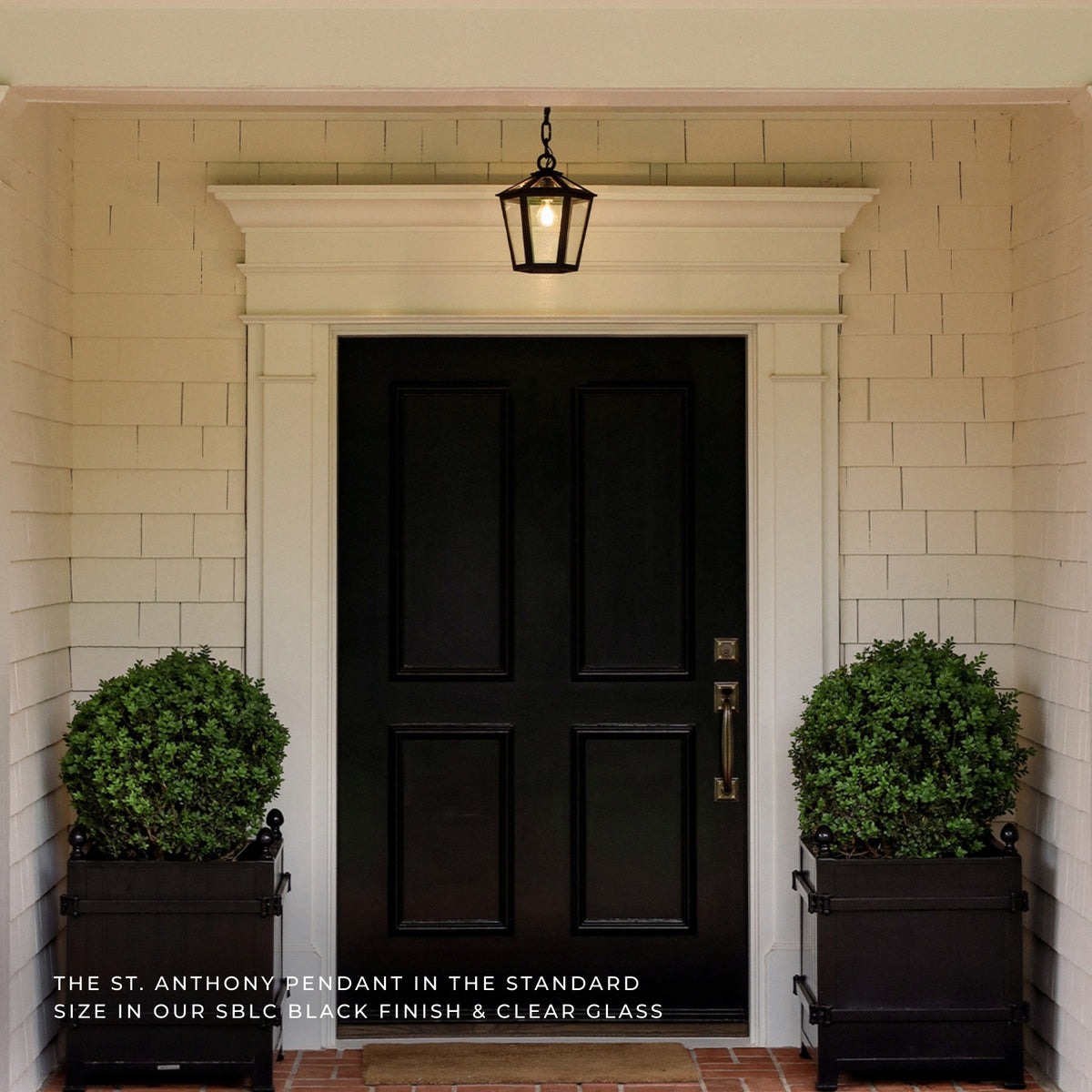 A black lantern-style pendant light hangs above a black front door on a white-shiplap porch, with two green planters on either side. Text at the bottom reads, 'THE ST.