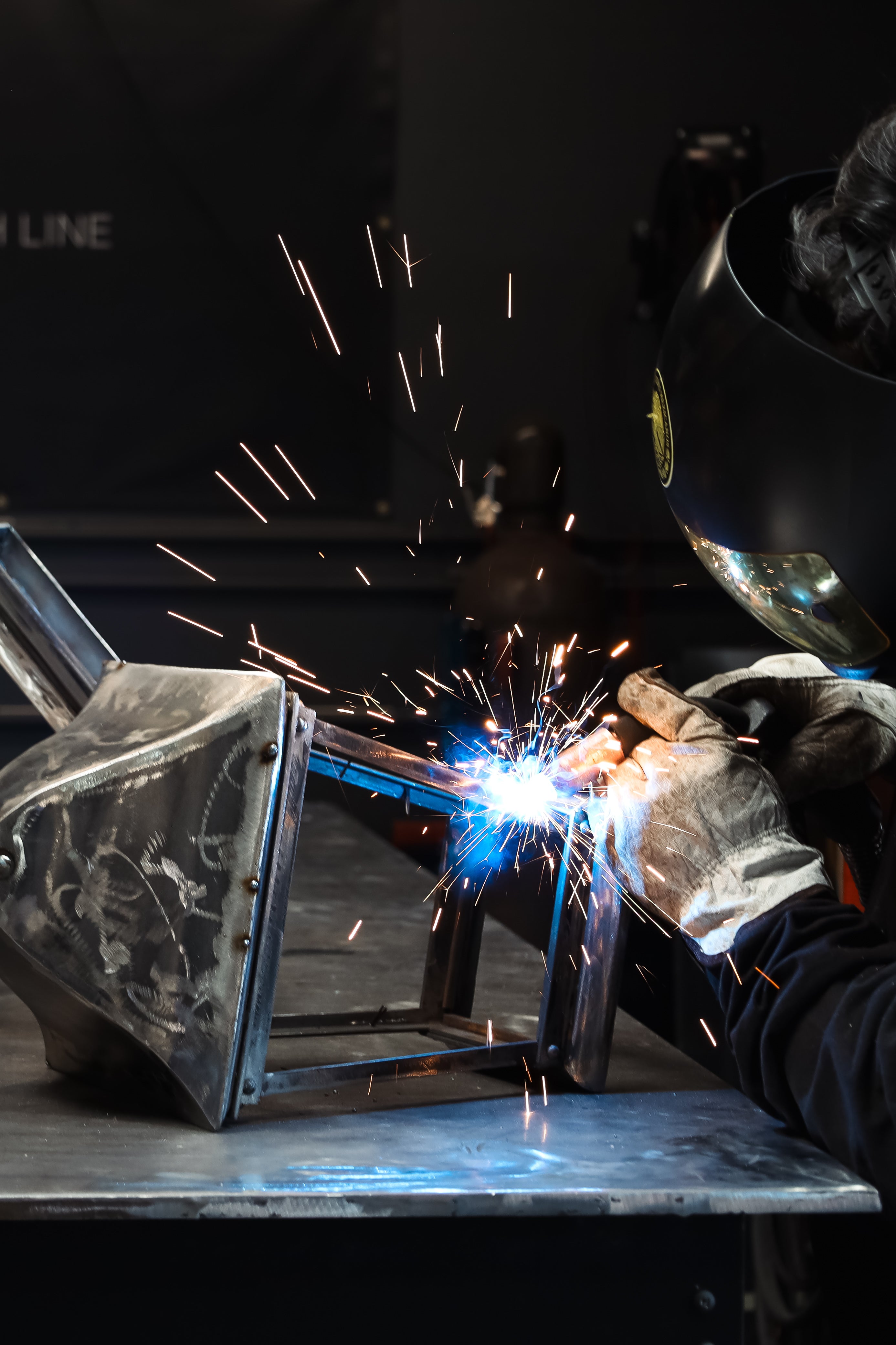 Person welding metal with sparks flying, wearing protective gear.