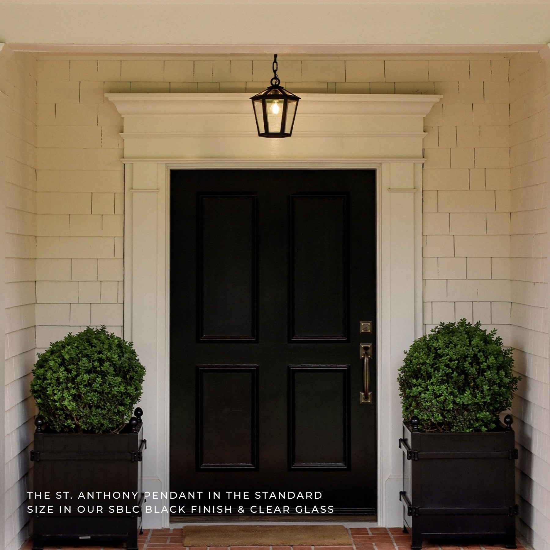 A black lantern-style pendant light hangs above a black front door on a white-shiplap porch, with two green planters on either side. Text at the bottom reads, 'THE ST.