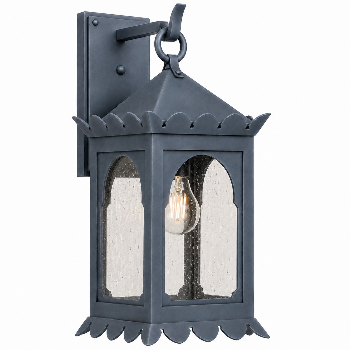 A dark gray metal outdoor wall sconce with a decorative lantern design, featuring scalloped trim, arched glass panels with seeded texture, and a visible warm-toned Edison bulb, shown against a plain white background.